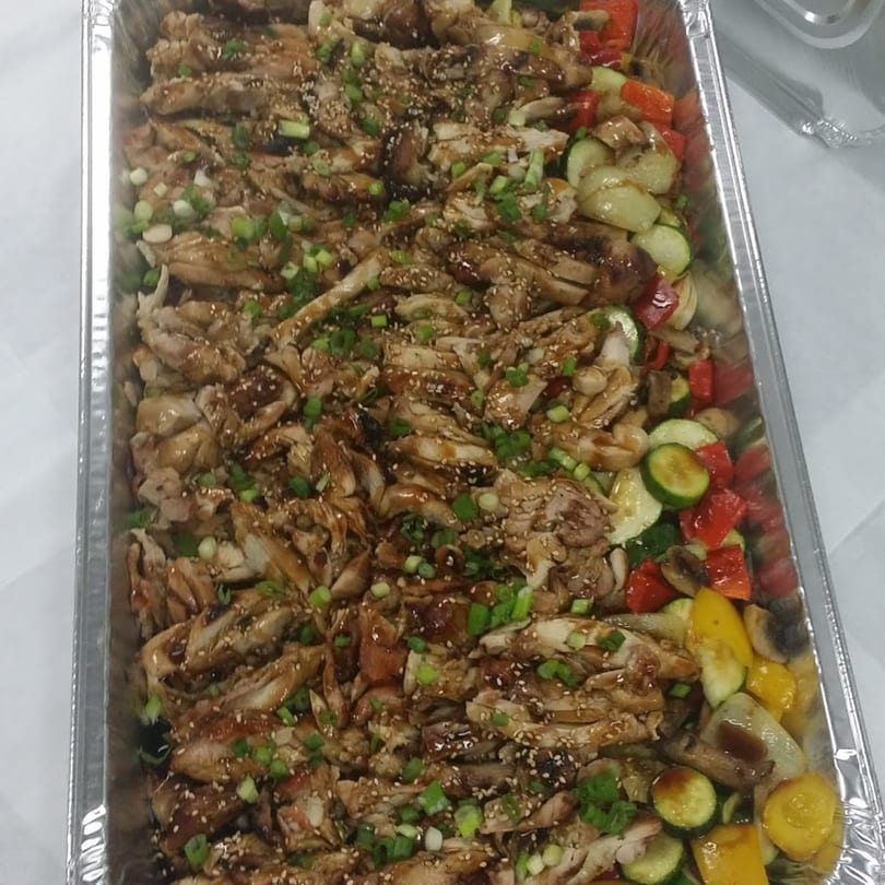 A catering tray of Sansai Japanese Grill's teriyaki chicken with sesame seeds, green onions, and mixed vegetables.