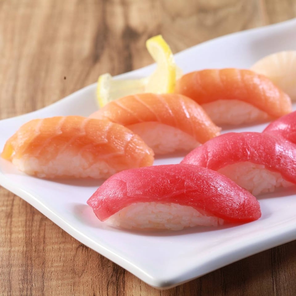 A white plate holds various pieces of salmon and tuna nigiri, garnished with lemon slices.