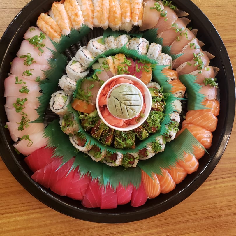 A large, circular platter of assorted sushi and sashimi, with wasabi and ginger in the center.
